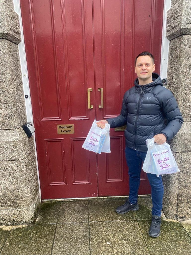 man holding oral health packs in front of red door which says Redruth Foyer