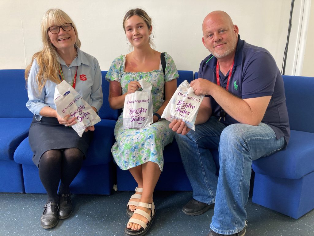 Grace sat in between lady and and man from Salvation army with oral health packs
