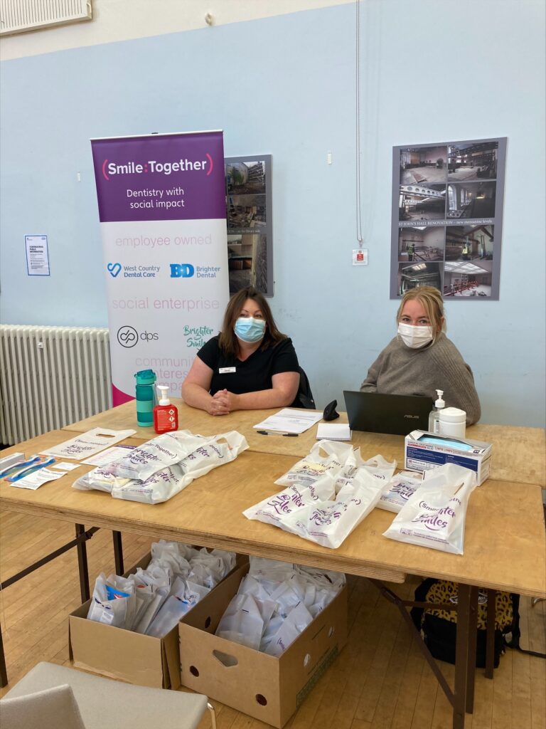 Two dental nurses seated at table with oral health packs