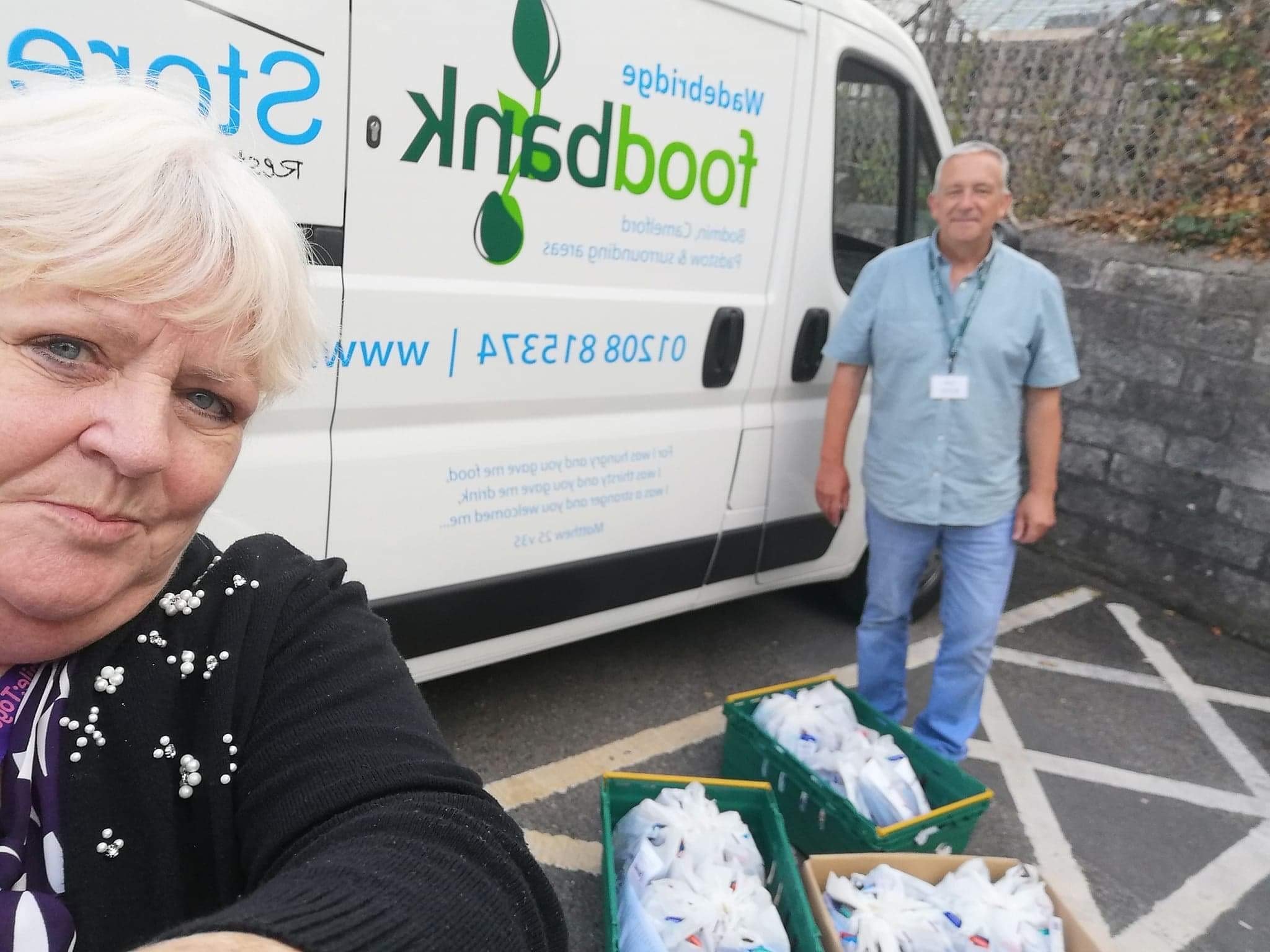 selfie of woman and man with three boxes of oral health packs outside wadebridge foodbank van