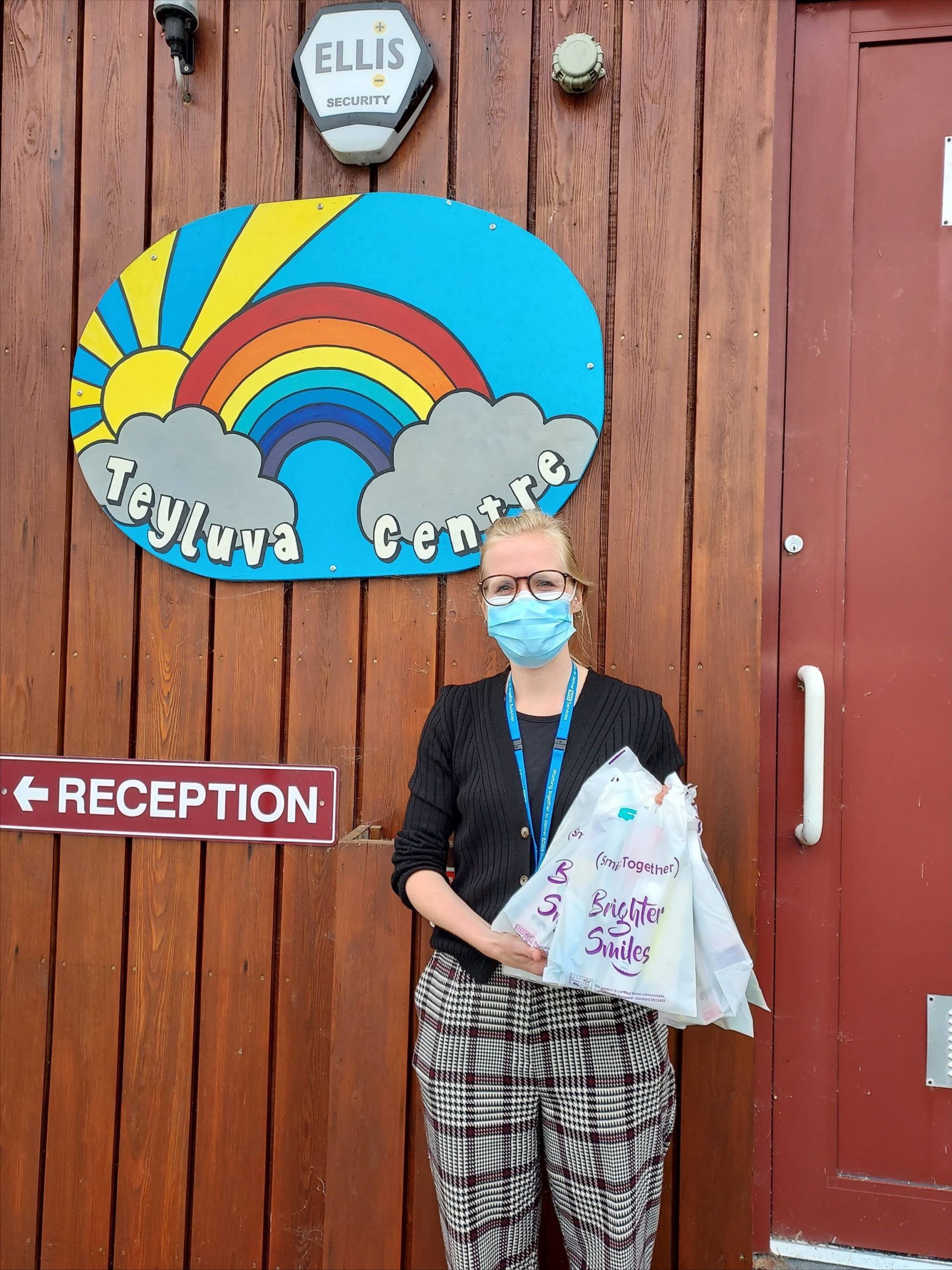 Woman masked holding oral health packs standing outside Teyluva Centre