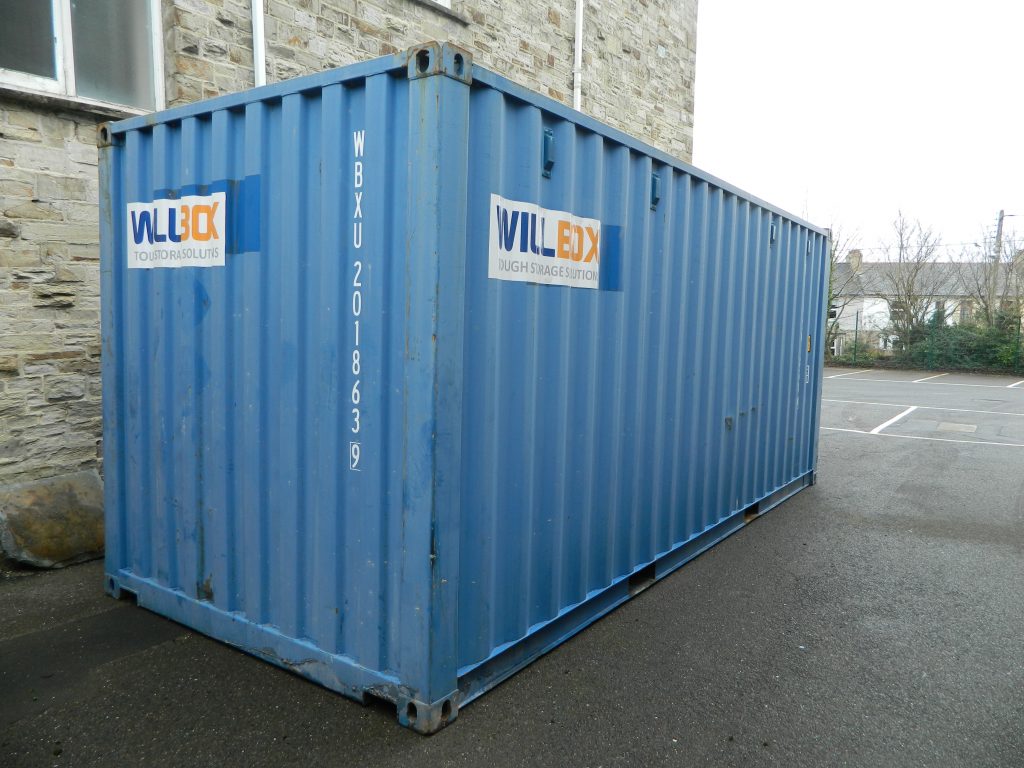 Blue 20ft shipping container in car park next to large stone building