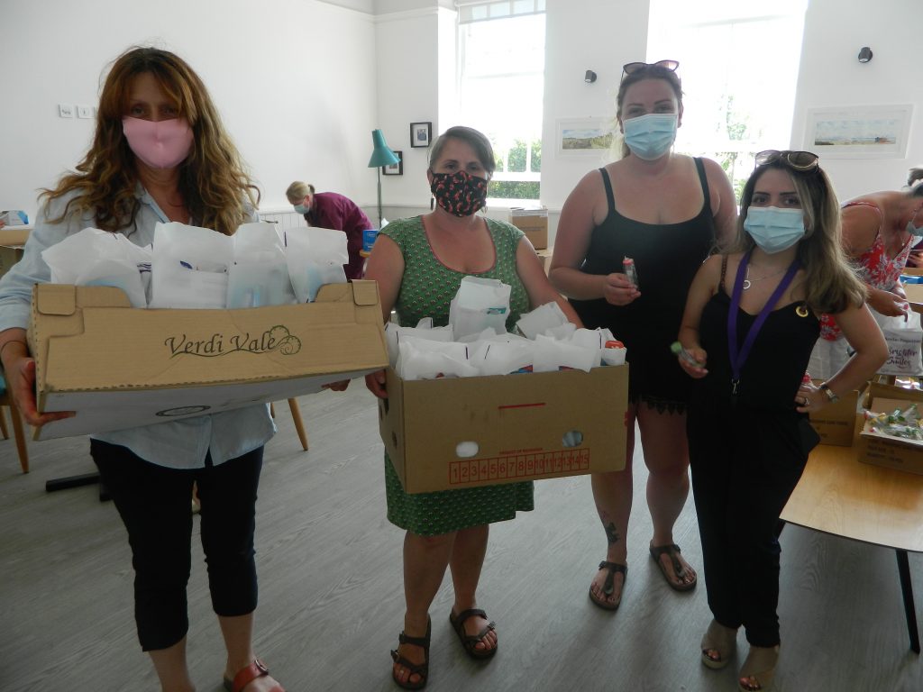 Four women masked standing in clinic holding boxes of oral health packs