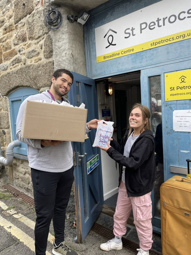 man holding box giving a lady an oral health pack in St Petrocs doorway