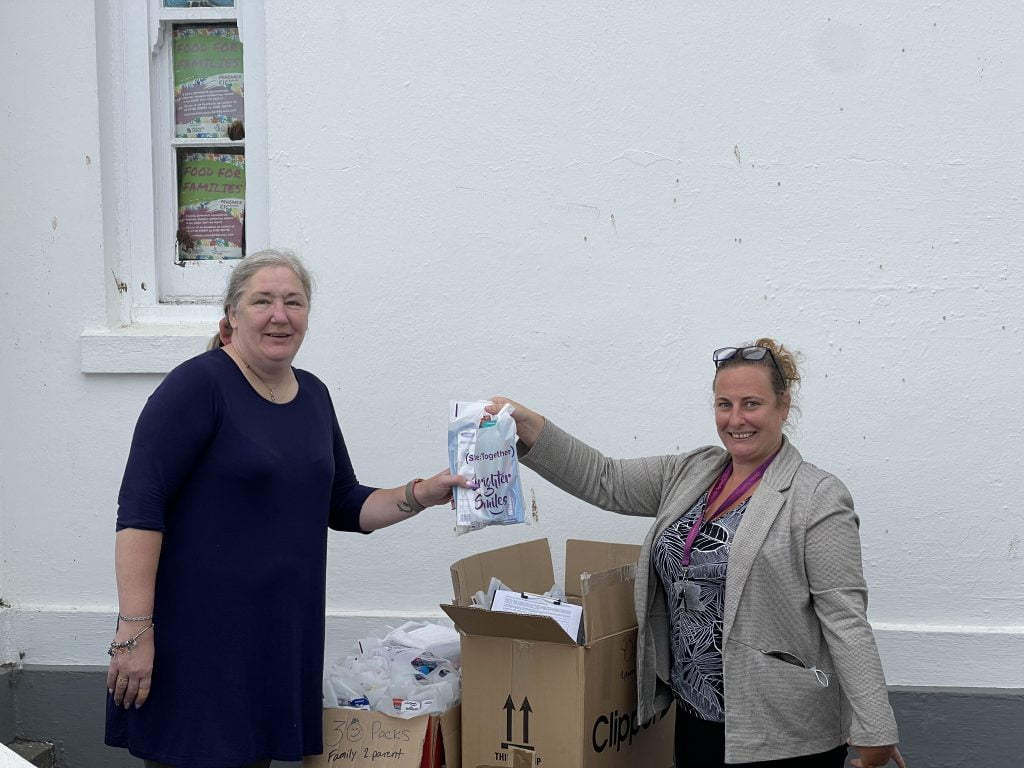 two ladies holding an oral health pack by two large boxes of packs