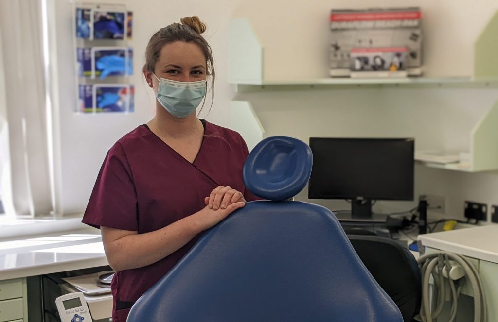 Dental nurse standing by dentist chair in clinic wearing mask