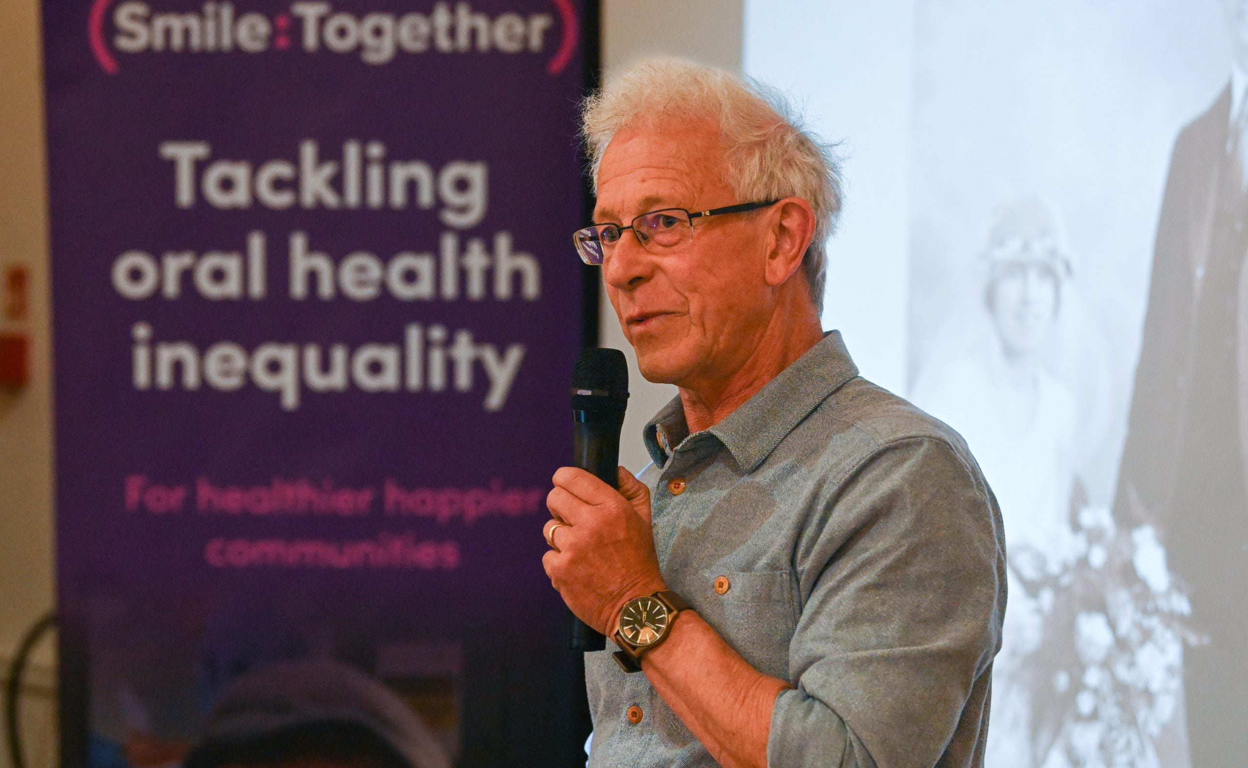 Chris Hines talking into mic with Smile Together 'tackling oral health inequality' poster in background