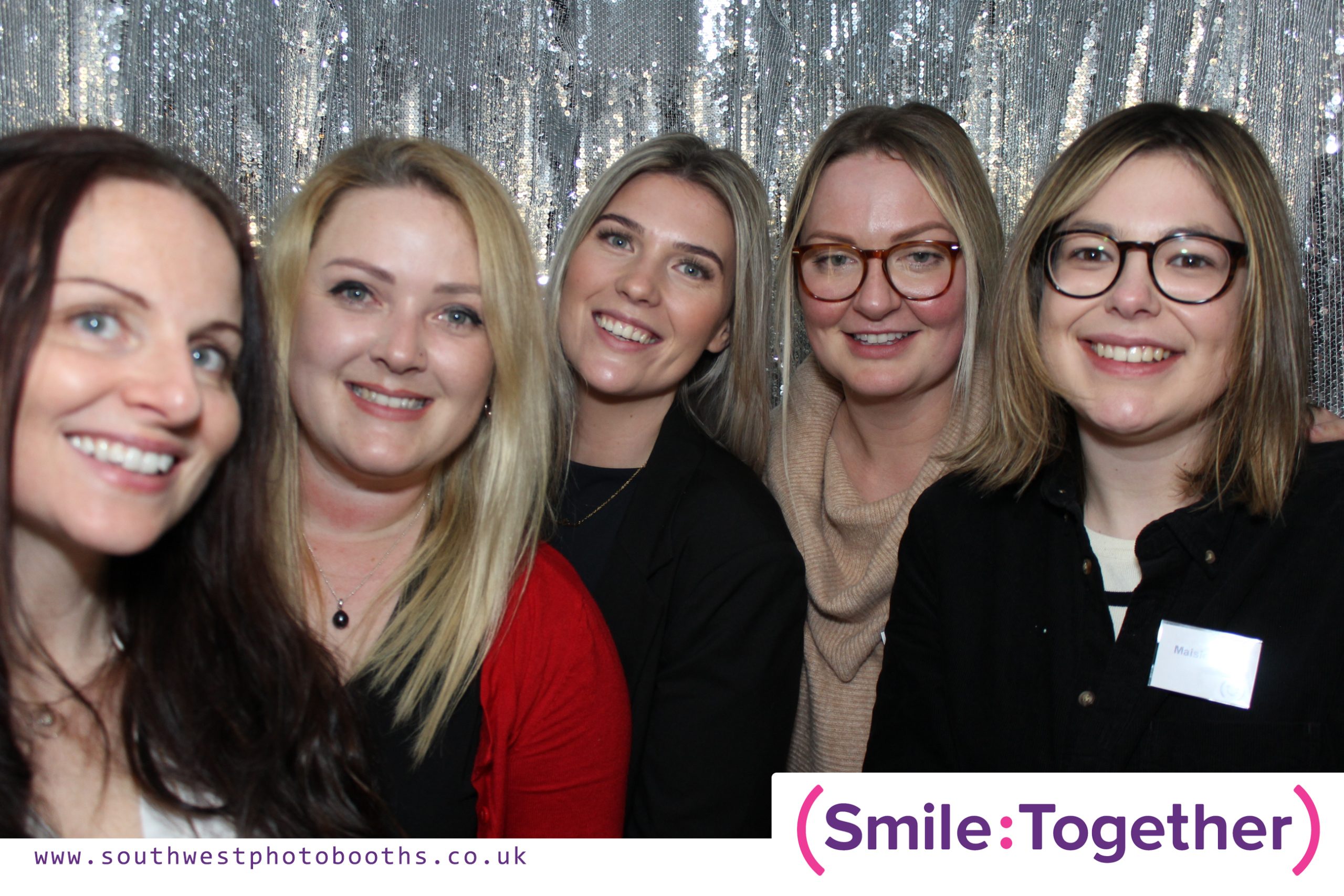 5 female colleagues in photo booth smiling with sequin curtain backdrop