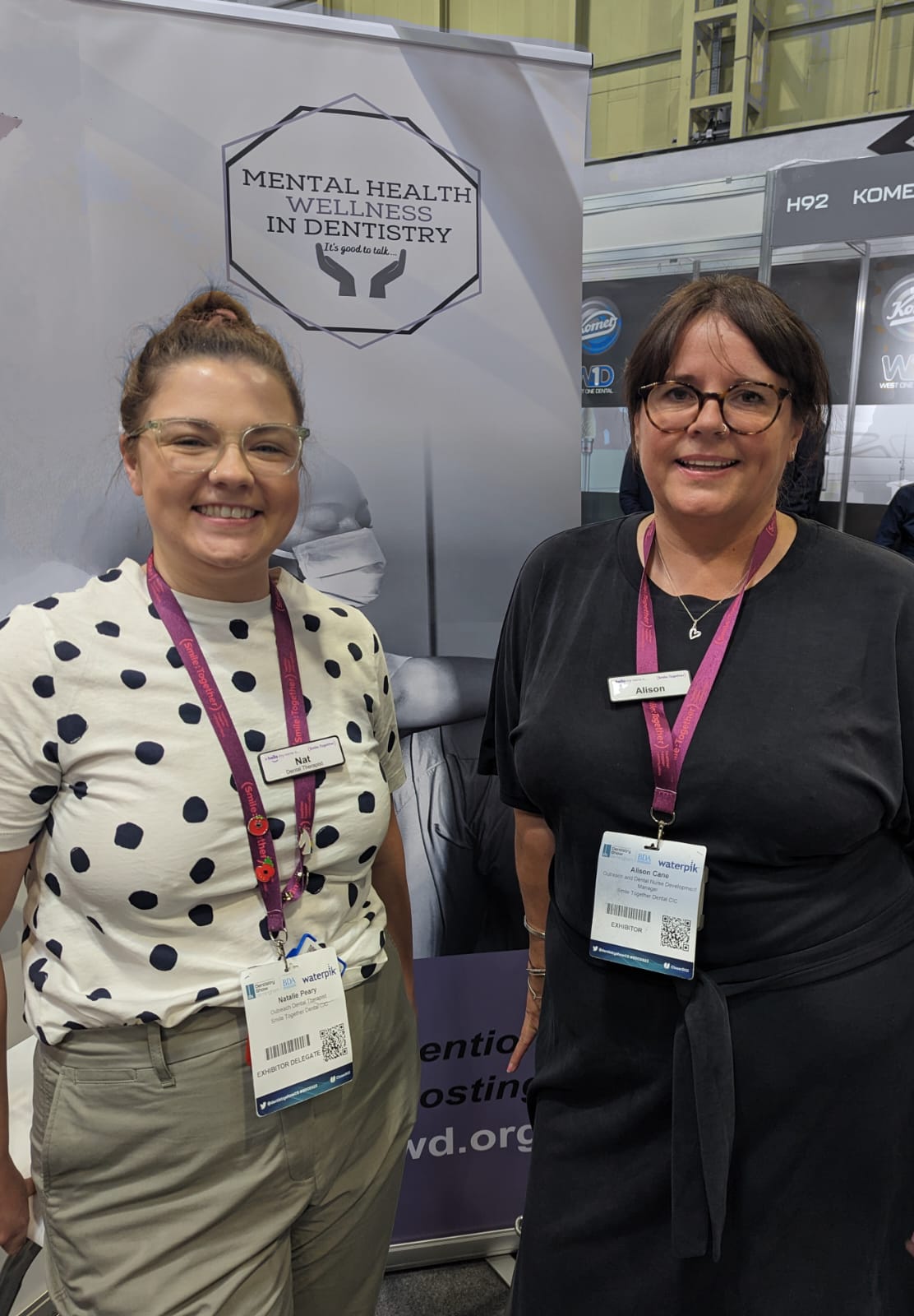 two female colleagues stood in front of 'Mental Health Wellness in Dentistry' poster