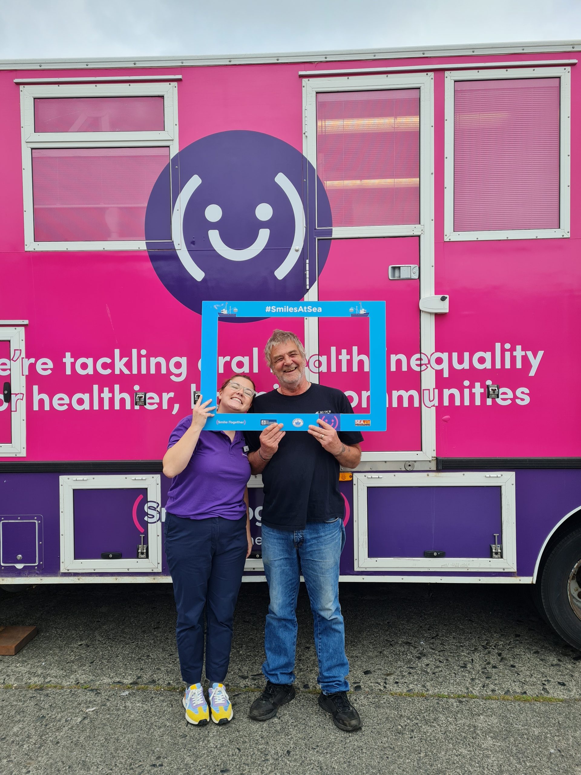 Smile Together colleague and fisherman holding frame in front of pink mobile dental unit
